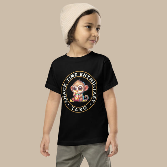 Toddler tee design featuring a cartoon tarsier named Taro eating chips from a bag with the words “Snack Time Enthusiast” in a circular badge-style layout.