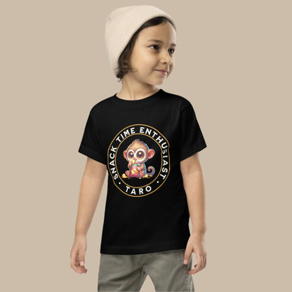 Toddler tee design featuring a cartoon tarsier named Taro eating chips from a bag with the words “Snack Time Enthusiast” in a circular badge-style layout.