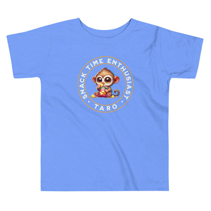 Toddler tee design featuring a cartoon tarsier named Taro eating chips from a bag with the words “Snack Time Enthusiast” in a circular badge-style layout.